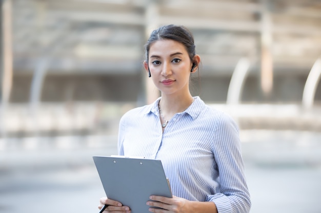 Portrait of confident female business people standing with clipboard against blurred background.