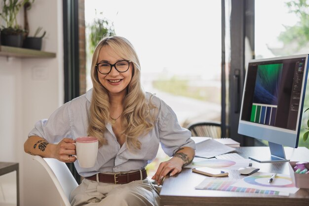 自宅からオンラインで仕事をしながら、コーヒーを飲みながらカメラを見る自信に満ちた女性フリーランスアーティストのポートレート。彼女には好きなことをする自由があります。