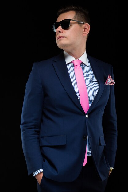 Photo portrait of confident handsome businessman in sunglasses on black background with hands in pockets