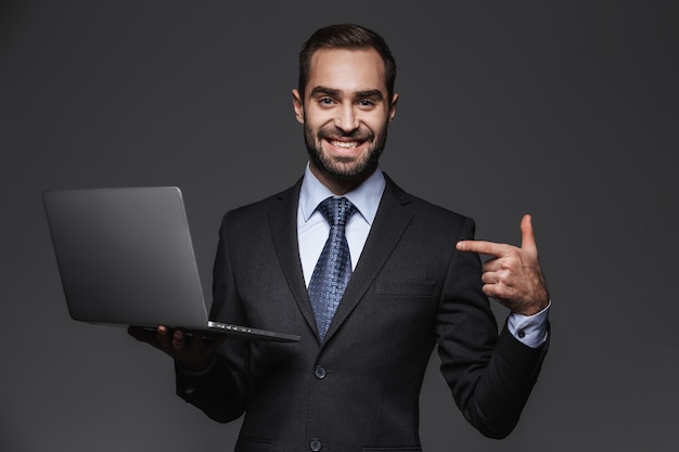 Portrait of a confident handsome businessman wearing suit isolated, holding laptop computer