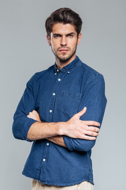 Portrait of a confident handsome man standing with arms folded isolated on the gray wall