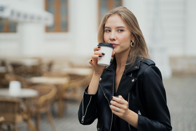 Photo portrait of a confident happy young blonde woman drinking coffee from a white paper cup