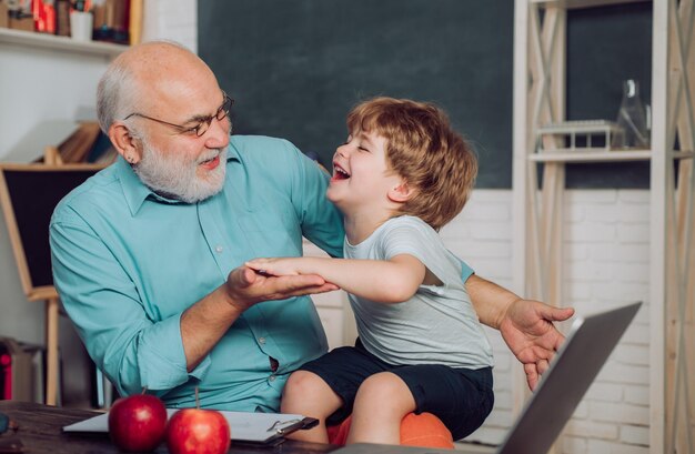 Portrait of confident old male teacher World teachers day Happy cute Grandson and Grandfather sitting at a desk indoors Educational process Grandfather with grandson learning together