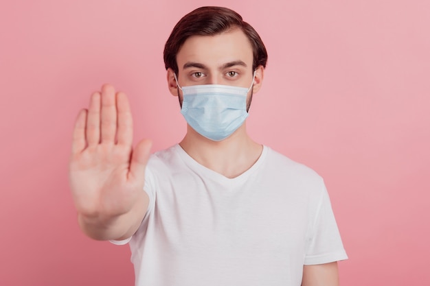 Portrait of confident protester guy wear medical mask raise hand show stop gesture on pink background