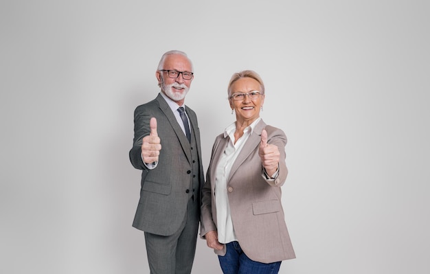 Portrait of confident senior colleagues showing thumbs up sign while standing over white background