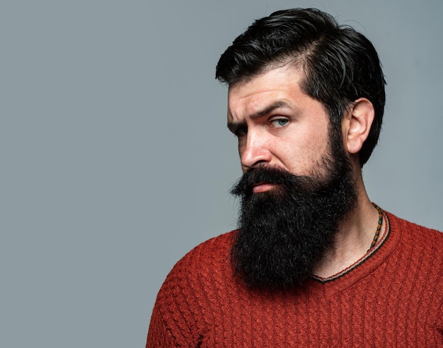 Portrait of confident serious man has beard and mustache, looks seriously, isolated on gray. Hipster guy models in studio.