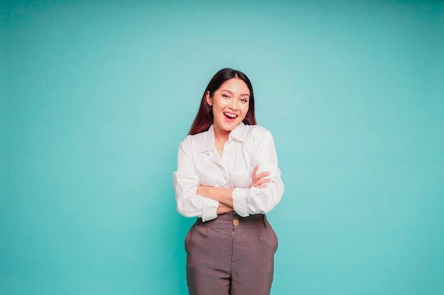 Portrait of a confident smiling Asian woman wearing white shirt standing with arms folded and looking at the camera isolated over blue background