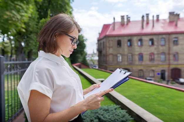 Portrait of confident smiling businesswoman female teacher counselor with clipboard paper documents Positive smiling woman copy space school building office building background