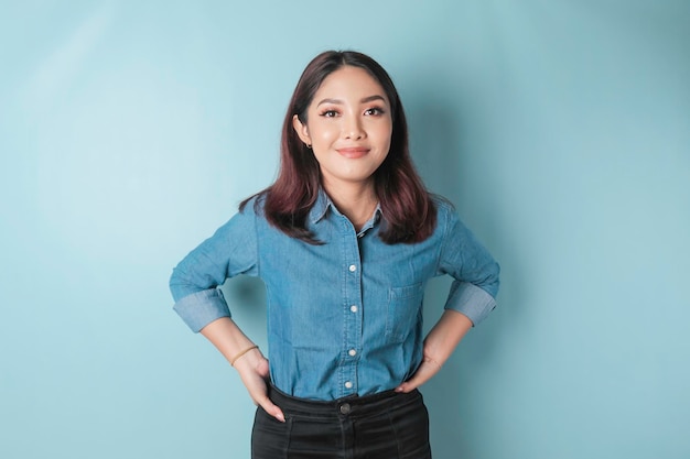 Portrait of a confident smiling girl standing with arms folded and looking at the camera isolated over blue background wearing a blue shirt