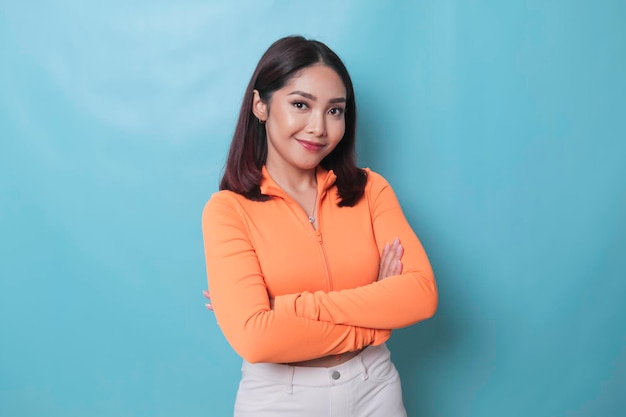 Portrait of a confident smiling girl standing with arms folded and looking at camera isolated over blue background