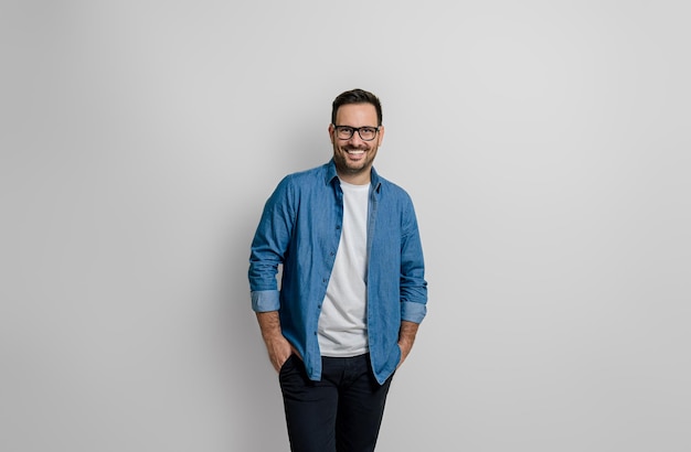 Portrait of confident smiling handsome businessman with hands in pockets posing on gray background