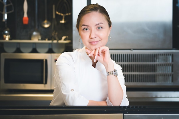 Portrait of confident and smiling young woman chef dressed in white uniform professional kitchen are on background