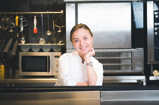 Photo portrait of confident and smiling young woman chef dressed in white uniform professional kitchen are on background