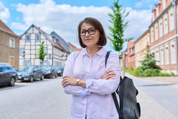Portrait of confident successful mature woman on street of European city Smiling beautiful middle aged female with crossed arms looking at camera
