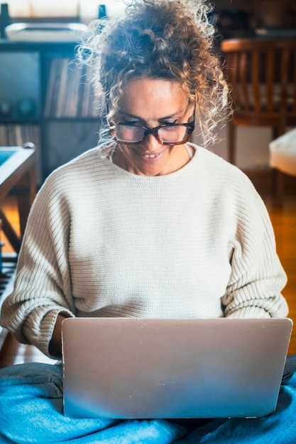 집에서 노트북으로 글을 쓰고 바닥에 앉아있는 자신감있는 여성의 초상화 실내 온라인 여가 활동 소셜 미디어 및 원격 작업 비즈니스 컴퓨터를 사용하고 미소 짓는 현대 여성