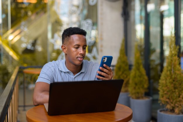 Portrait of confident young African businessman wearing casual clothes and using mobile phone