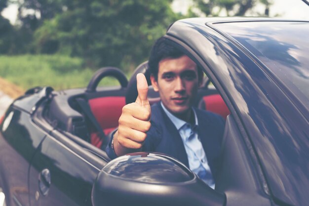 Photo portrait of confident young businessman showing thumbs in car on road