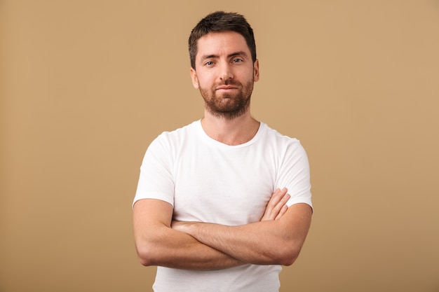 Portrait of a confident young man casually dressed standing isolated over beige