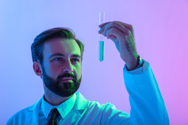 Портрет уверенного в себе молодого человека-ученого в пальто, стоящего изолированно над розово-голубой дымкой, показывая медицинскую трубку с жидкостью
