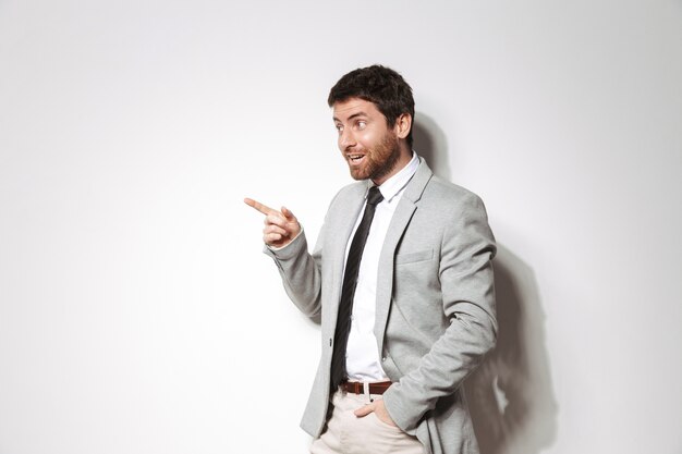 Portrait of a confident young man wearing suit standing isolated, pointing at copy space