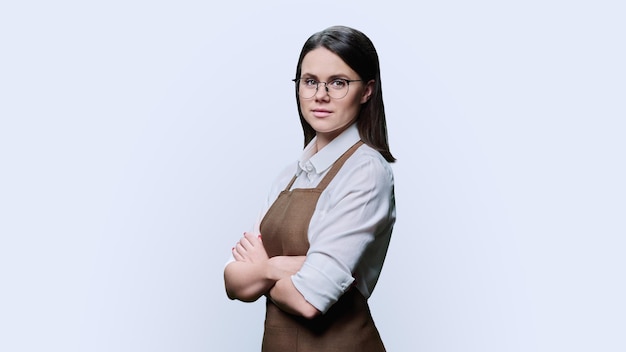 Portrait of confident young woman worker in apron on white studio background Successful smiling female service worker small business owner salesperson in uniform with crossed arms looking at camera