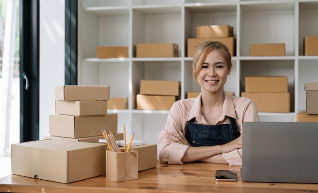 Portrait of a confidential asian woman waitress apron sitting at her home with cardboard for shipping online shopping small business owner concept