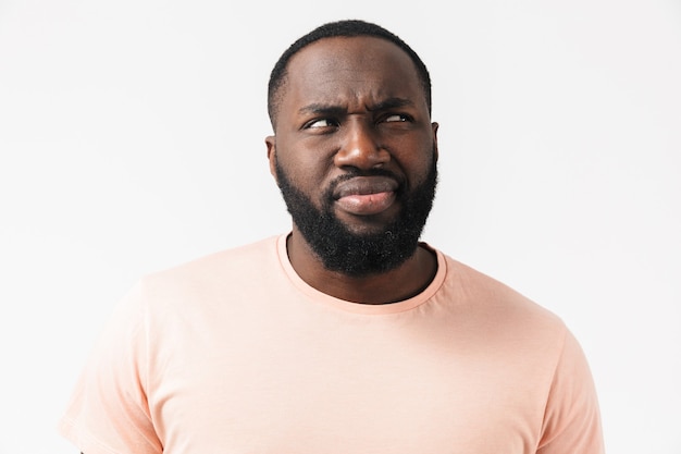 Portrait of a confused african man wearing t-shirt standing isolated over white wall, grimacing