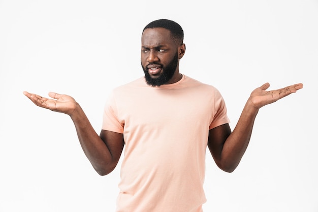 Portrait of a confused african man wearing t-shirt standing isolated over white wall, shrugging shoulders