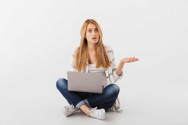 Portrait of confused young casual woman with laptop computer