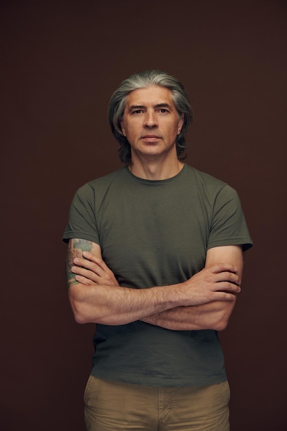 Portrait of contemplative handsome mature man with tattoo on arm rubbing chin while posing against b