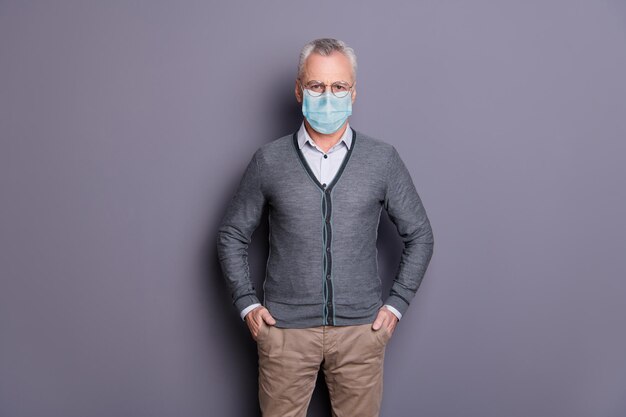 Portrait of content man wearing mask casual formal-wear holding hands in pockets isolated over gray pastel background