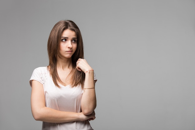 Portrait of contused thinking brunette woman. Studio shot on gray background.