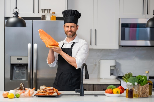 Ritratto di uomo cuoco che prepara salmone fresco in cucina bell