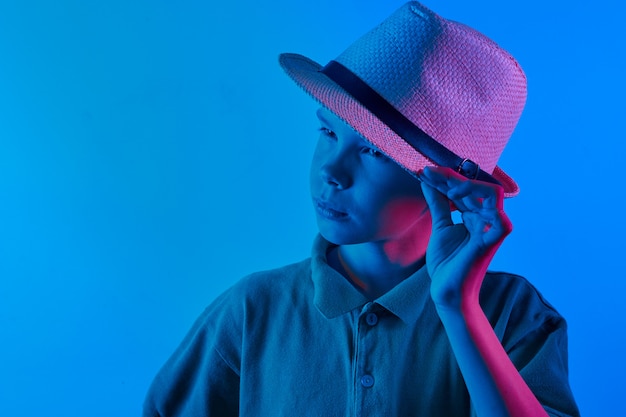Portrait of a cool boy child stylishly posing in a straw hat on a blue and violet neon light. Toned. Colored.