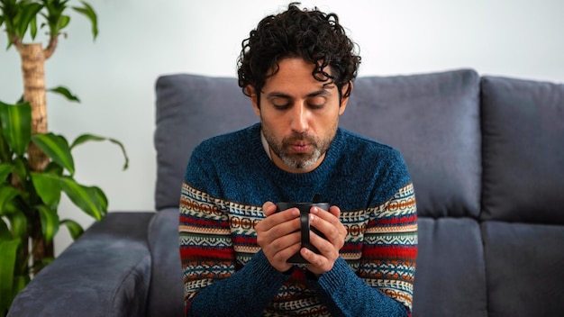 Portrait of cool and handsome man drinking morning expresso coffee and sitting on a couch at home interior. A person is resting and looking away.