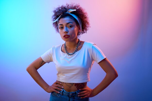 Portrait of cool Kazakh girl with curls and tattoo posing in neon light isolated on studio background