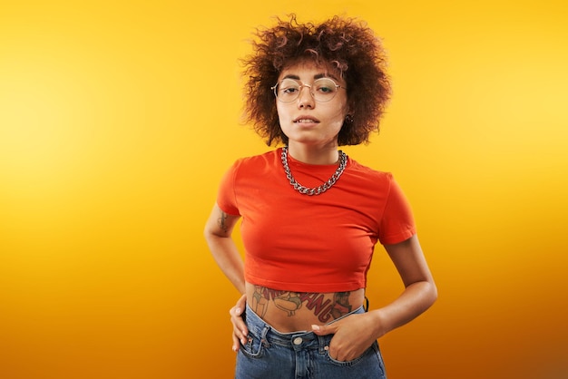 Portrait of cool Kazakh model girl with curls tattoo and chain posing isolated on yellow studio background