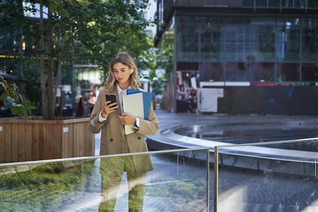 Portrait of corporate woman in suit using mobile phone waiting
for business partner in city center h