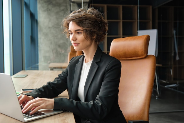 Photo portrait of corporate woman in suit working in office using laptop typing does her job in coworking