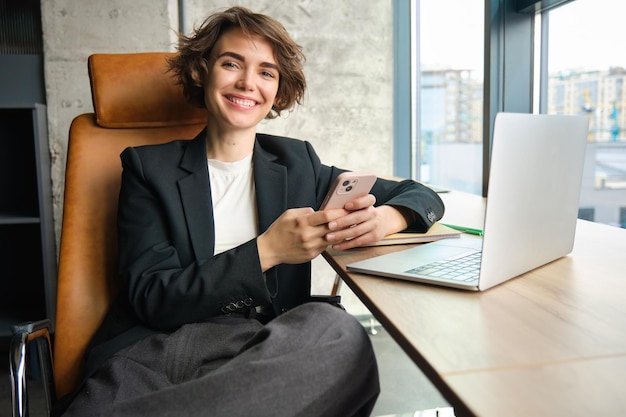 Photo portrait of corporate woman working in her office answering to messages on smartphone sitting with