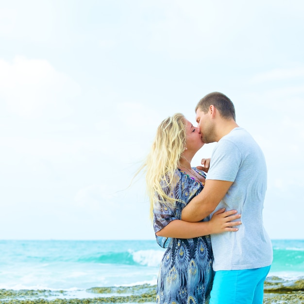 Portrait of a couple in casual clothing kissing on the beach at summer time