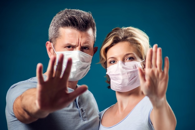 A portrait of couple of man and woman with face medical mask showing stop gesture. People, healthcare and medicine concept