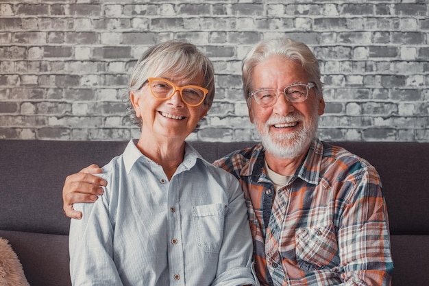 Photo portrait of couple of mature people wearing glasses and looking at the camera together close up of two seniors sitting on the sofa having fun and enjoyingxa