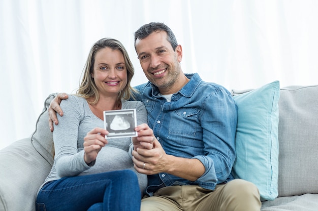 Portrait of couple sitting on sofa and holding ultrasound scan