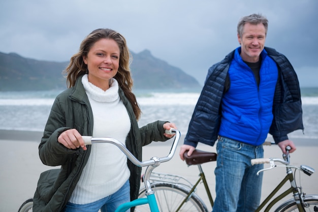 Portrait of couple standing with bicycle on beach