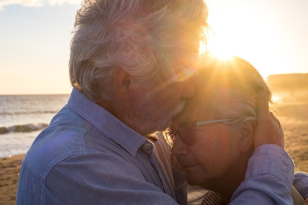 一緒にビーチで2人の幸せな先輩と成熟した老人のカップルの肖像画。年金受給者と引退した男が泣いている悲しい落ち込んでいる妻を慰めます。