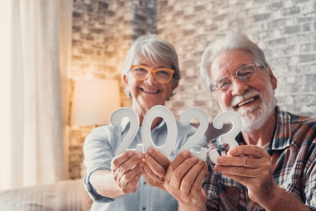 自宅で 2023 年の数字を一緒に保持している 2 人の古い年金受給者のカップルの肖像画 祝う新年の数字と新しい生活の概念の目標のクローズ アップ