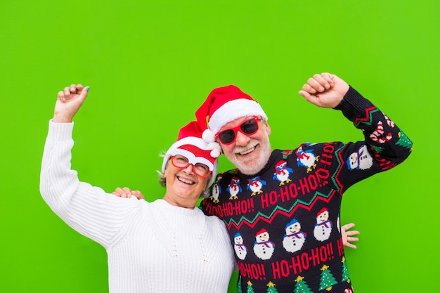 Portrait of couple of two seniors and mature and old people having fun enjoying christmas day together wearing christmas clothes and with green colorful background