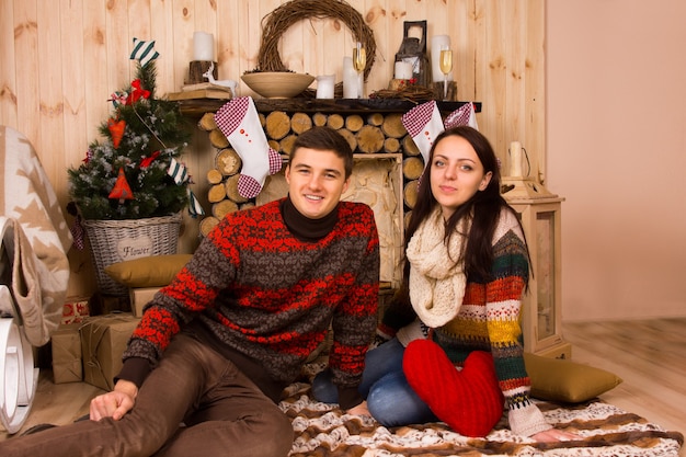 冬にログキャビン内の床に座っているセーターを着ているカップルの肖像画