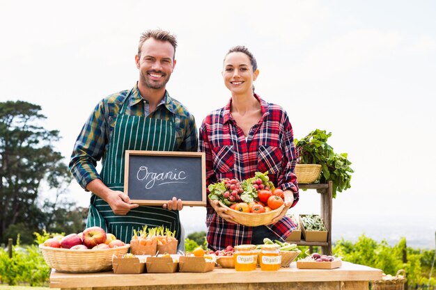 Portrait of couple with blackboard and basket selling vegetables